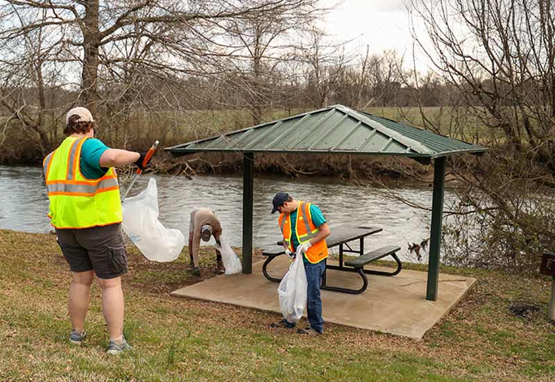 Volunteers pick up trash at picnic area by a stream
